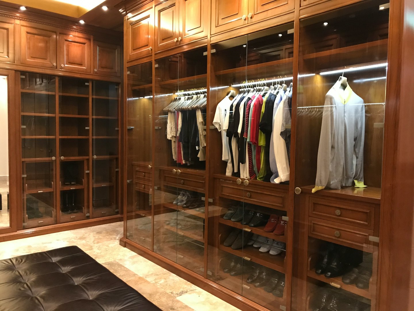 Spacious walk-in closet with dark wood cabinets and leather bench.