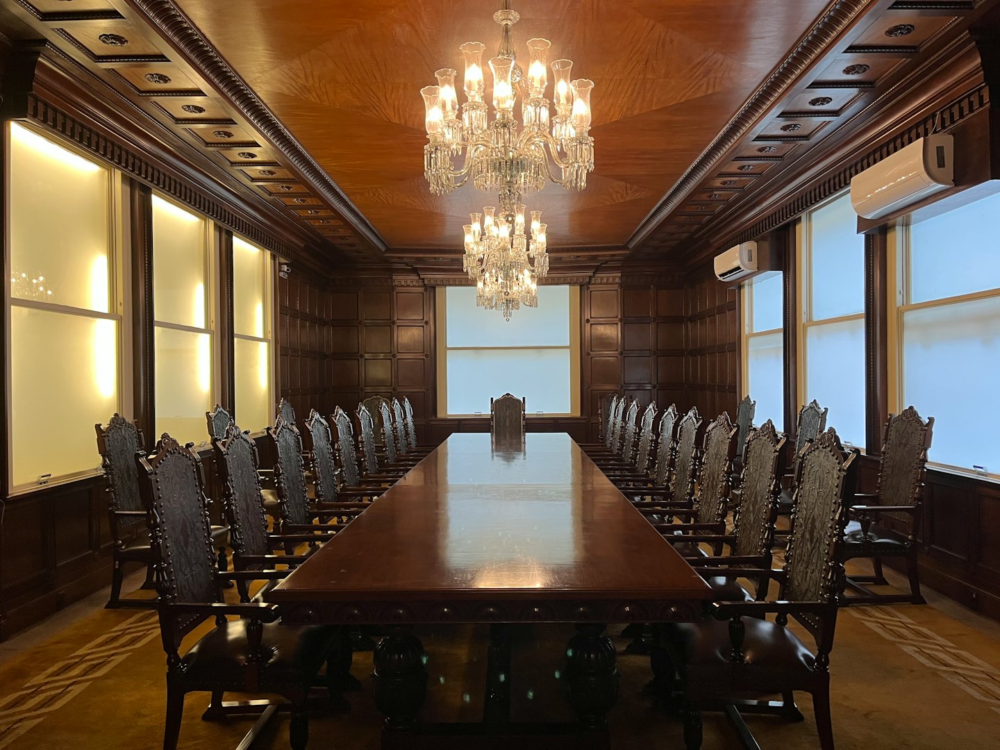 Empty boardroom with polished conference table and ornate chairs.
